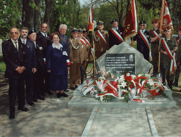 Grupa osób, w tym poczet sztandarowy,  przy pomniku poświęconym pamięci Sybiraków